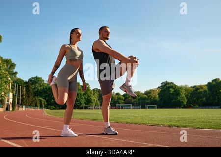 Junge sportliche Männer und Frauen in Sportbekleidung, die sich unter der Morgensonne auf der Laufbahn Strecken. Konzept von Fitness, Aufwärmen und gesundem Lebensstil. Stockfoto