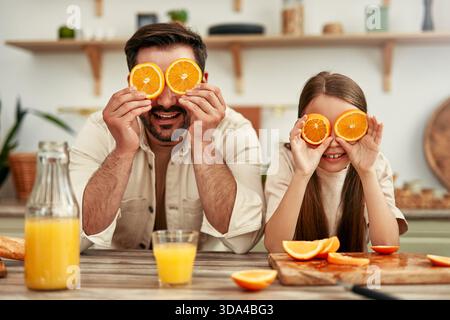 Eine glückliche Familie schafft fröhliche Erinnerungen in der Küche, verbindet sich mit verspielten Momenten mit Orangenscheiben, pflegt Beziehungen und genießt jeden einzelnen Stockfoto