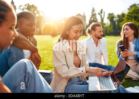 In einem wunderschönen, sonnigen Park verbindet sich eine vielfältige Gruppe von Freunden, um zu lernen, sich zu entspannen, Ideen auszutauschen, zu lachen und ein Gefühl der Gemeinschaft zu schaffen Stockfoto