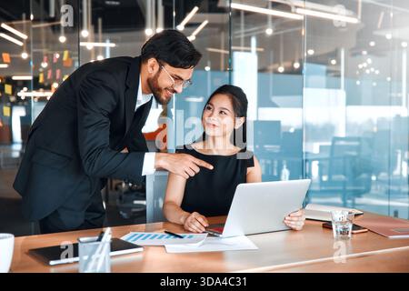 Menschen, die in einem Coworking-Raum arbeiten. Zwei Geschäftsmitarbeiter diskutieren zukünftige Strategien und Pläne, während sie in einem modernen Büro an einem Laptop sitzen. Stockfoto