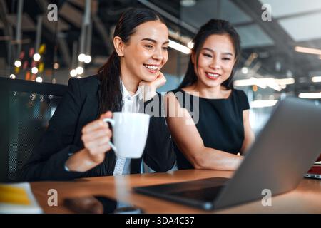 Ein Team junger Geschäftsleute in formellen Anzügen arbeitet mit Laptops, während sie in einem modernen Büro sitzen. Geschäftsfrauen, die an Laptops arbeiten und über ein Bu diskutieren Stockfoto