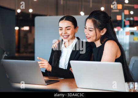 Ein Team junger Geschäftsleute in formellen Anzügen arbeitet mit Laptops, während sie in einem modernen Büro sitzen. Geschäftsfrauen, die an Laptops arbeiten und über ein Bu diskutieren Stockfoto