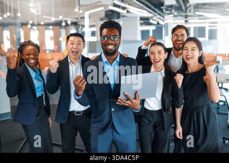 Ein Team erfolgreicher Geschäftsleute verschiedener Nationalitäten in Anzügen feiert den Sieg und Erfolg in einem modernen Büro. Stockfoto