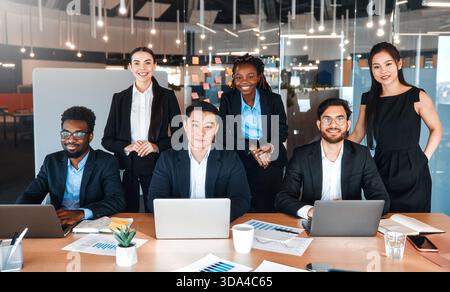Team erfolgreicher junger Geschäftsleute in formellen Anzügen mit Laptops im modernen Büro. Junge Menschen unterschiedlicher Nationalitäten, die in einem Coworkin arbeiten Stockfoto