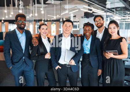 Team erfolgreicher junger Geschäftsleute in formellen Anzügen mit Laptops im modernen Büro. Junge Menschen unterschiedlicher Nationalitäten, die in einem Coworkin arbeiten Stockfoto