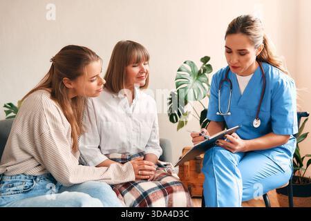 Hausarzt zu Hause untersucht eine ältere Frau, die mit ihrer Tochter im Wohnzimmer auf dem Sofa sitzt. Patientenuntersuchung, Gesundheitswesen und Medizin Stockfoto