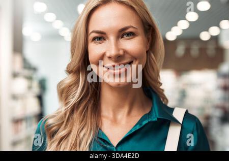 Porträt einer lächelnden blonden Frau in blaublauer Bluse im Schönheitsgeschäft. Sie sieht glücklich und selbstbewusst aus. Konzept: Natürliche Schönheit und Kundenzufriedenheit. Stockfoto
