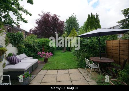 Grüner Gartenbereich mit Sitzgelegenheiten und schattigem Tisch unter bewölktem Himmel in kleinem Außenbereich Stockfoto