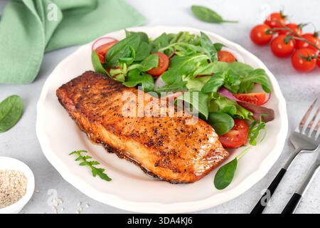 Gegrilltes Lachsfilet mit frischem Salat aus Kirschtomaten, Spinat und Blattgemüse. Gesunde ausgewogene Mahlzeit. Stockfoto