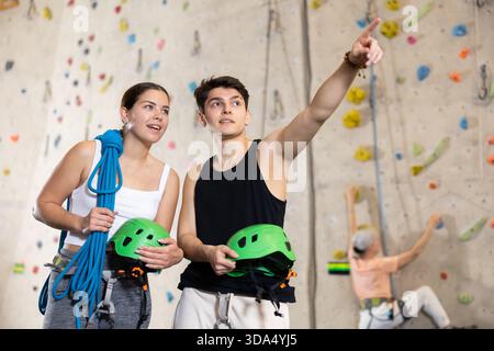 Motivierte, sportliche Jugendliche, Mann und Frau, die mit Spezialausrüstung stehen, bevor sie im Vergnügungszentrum die Boulderwand hochklettern Stockfoto