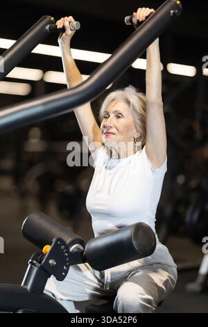 Ältere Frau, die im Fitnessstudio auf einem Lat Pulldown-Gerät trainiert Stockfoto