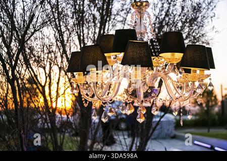 Hängender Kronleuchter, der bei einer Veranstaltung im Freien in der Abenddämmerung von einem Baum hängt Stockfoto
