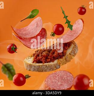 Satz fliegende, geschnittene frische Wurst auf orangefarbenem Hintergrund. In Scheiben geschnittene Salami fallen. Stockfoto