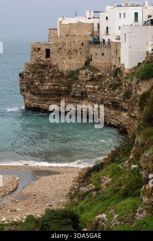 Die historischen weißen Gebäude und Steinbefestigungen von polignano a Mare, apulien, italien, stehen auf steilen Klippen über einem kleinen Kieselstrand und der Stockfoto
