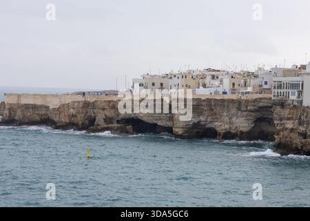Bezaubernde weiß getünchte Gebäude von Polignano a Mare auf dramatischen Kalksteinklippen mit Blick auf die Adria unter bewölktem Himmel Stockfoto
