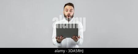 Mann in weißem Hemd reagiert überrascht auf Laptop-Bildschirm in Studio-Einstellung Stockfoto