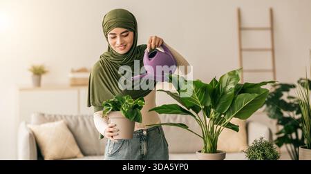 Junge Frau bewässert die Pflanzen in der Halle, während sie die Zeit zu Hause in einem sonnigen Wohnzimmer genießt Stockfoto