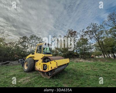 Gelbe Straßenwalze, kleines Modell, auf einer Wiese ausgestellt. Eine Straßenwalze oder Verdichterwalze wird für Asphalt und Straßenrenovierung und -Bau verwendet. Stockfoto