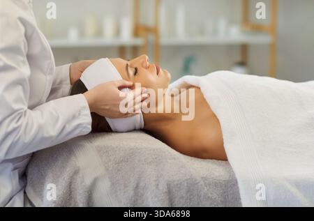 Junge Frau liegend mit geschlossenen Augen, genießt Gesichtsmassagen und Hautpflegebehandlungen im Spa-Salon. Stockfoto