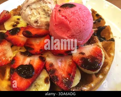 Frisch gebackene Waffeln mit Erdbeerscheiben, Bananen, Schokoladensirup und Schaufeln Erdbeeren- und Vanilleeis, die ein dekadentes de schaffen Stockfoto