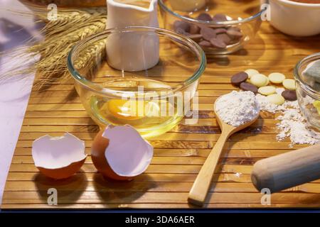 Backzutaten einschließlich Eiermehl und Schokoladenchips auf einer Bambusmatte mit Werkzeugen. Stockfoto