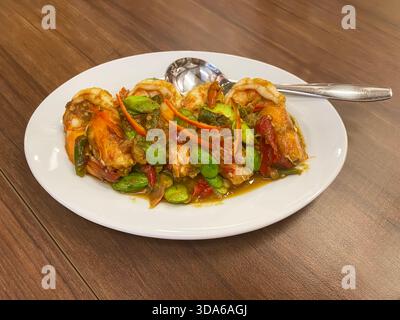 Scharfe gebratene Garnelen mit Stinkbohnen und Garnelenpaste auf weißem Teller auf Holztisch. Stockfoto