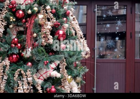 Farbenfrohe Dekorationen auf einem Weihnachtsbaum bringen Freude und Wärme in eine verschneite Szene. Stockfoto