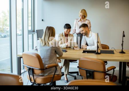 Gruppe von Fachleuten, die in einem modernen Büro Teamarbeit leisteten und Ideen diskutierten, während sie ein Tablet um einen Holztisch herum benutzten. Stockfoto
