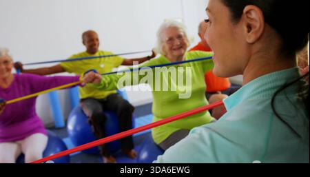 Führender Trainer mit rotem Band im Studio mit Klasse auf blauen Stabilitätsbällen mit hellen Oberteilen Stockfoto