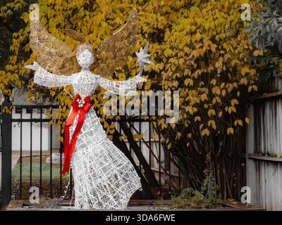 Drahtenengel mit einem leuchtend roten Bogen hält einen Stern vor goldenem Herbstlaub, einem fröhlichen Feiertagshof. Stockfoto