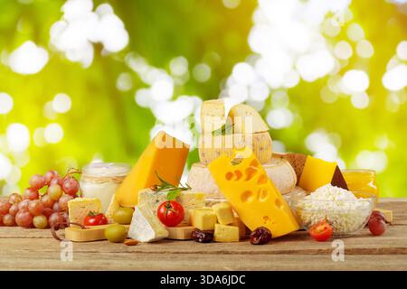 Verschiedene Käsesorten und frisches Obst auf einem Holztisch in sonniger Umgebung Stockfoto