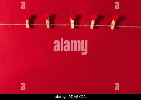 Roter Hintergrund mit herzförmigen Clips, die zur Dekoration an einer Schnur hängen Stockfoto