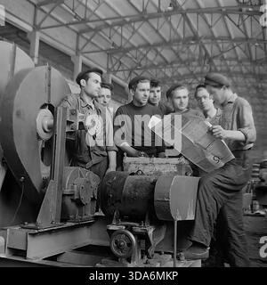 Slawjansk, Ukrainische SSR, UdSSR - 1970er Jahre: Eine Brigade sowjetischer Arbeiter in der Montagewerkstatt der Stroymash-Fabrik, die während einer Pause die Prawda-Zeitung liest. Die Männer in Arbeitskleidung und Baskenmützen versammeln sich um einen großen industriellen Zentrifugalfan und diskutieren über die neuesten Nachrichten. Dieses Schwarzweiß-Archivfoto fängt die Atmosphäre des politischen Bewusstseins und des kollektiven Lebens der friedlichen Donbass-Region während der Sowjetzeit ein. Das Produktionsteam für schwere Industriemaschinen nimmt eine kurze Pause ein. Stockfoto