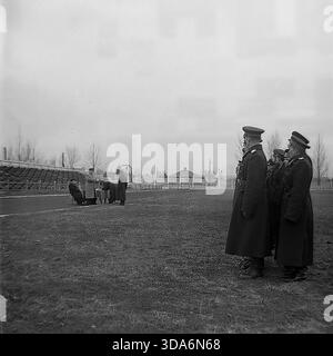 Slawjansk, Ukrainische SSR, UdSSR - 1956: Feierliche Eid-Ablegung der sowjetischen Milizoffiziere im Khimik-Stadion. Hochrangige Offiziere stehen an einem Tisch auf der Laufbahn und lesen den Text des Eid auf die Bildung von Polizisten in Wintermänteln. Im Hintergrund ist die Stadiontribüne mit Balustraden zu sehen. Dieses schwarz-weiße Archivfoto zeigt die offizielle Atmosphäre der Strafverfolgung und der Staatsmacht in der friedlichen Donbass-Region während der Sowjetzeit. Stockfoto