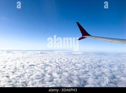 Flügel aus dem Flugzeugfenster an bewölktem Tag. Luftaufnahme von Wolken durch ein ebenes Fenster. Flügel eines Flugzeugs mit Nebelwolken Stockfoto