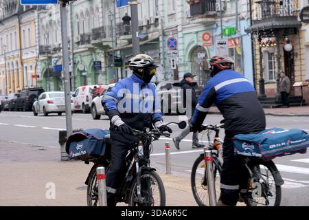Zwei Radfahrer in Winterkleidung fahren auf einer belebten Stadtstraße und liefern Pakete. Podil, Kiew, Ukraine. Dezember 2025. Stockfoto