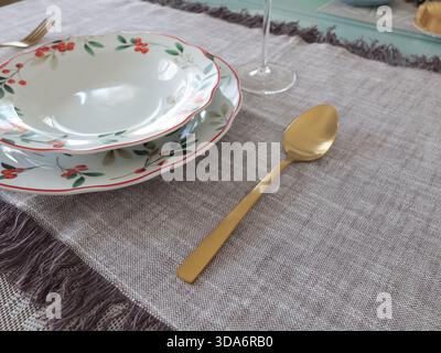 Goldener gelber Löffel neben Suppen- und Tellern mit Blumenmuster auf dem Tisch. Essen und Tischaufstellung. Keramikgeschirr. Stockfoto