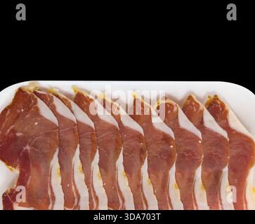 Jamon serrano. Ein spanischer Schinken, isoliert auf schwarzem Hintergrund. Traditioneller spanischer Jamon in Scheiben. Trocken gepökelter Fleischschinken. Hamon iberico Stockfoto