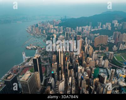 Aus der Vogelperspektive werfen die Wolkenkratzer lange Schatten in die pulsierende Stadtlandschaft von Hong Kong Island, im Kontrast zum ruhigen Wasser des harb Stockfoto