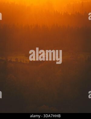 Blick aus der Vogelperspektive auf ein einsames Haus inmitten einer goldenen, trüben Landschaft, getaucht im warmen Glanz der untergehenden Sonne, Saint-Hymer, Normandie, Frankreich. Stockfoto