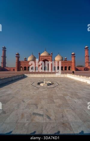 Blick auf den großen Innenhof der Badshahi Moschee und die riesigen Minarette vor klarem Himmel, in warmes Sonnenlicht getaucht, Lahore, Lahore, Pakistan. Stockfoto