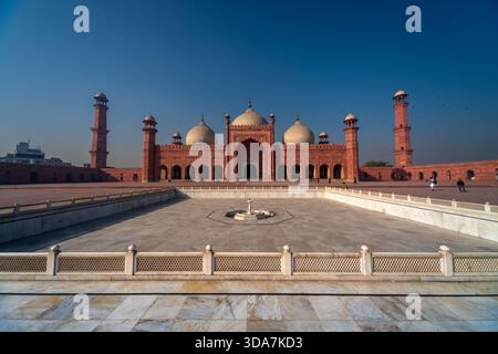 Der Blick auf die rote Sandsteinfassade der Badshahi-Moschee erhebt sich majestätisch unter einem klaren blauen Himmel, deren Kuppeln und Minarette in Lahore, Pakista, glitzern Stockfoto