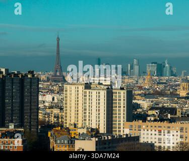 Blick aus der Vogelperspektive auf den Eiffelturm, der die Skyline durchquert, inmitten einer weitläufigen Stadtlandschaft mit verschiedenen architektonischen Stilen, getaucht in den sanften Glanz eines Winters Stockfoto