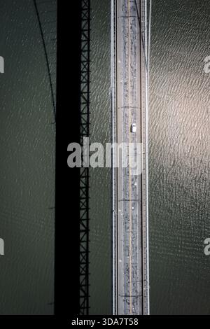 Aus der Vogelperspektive auf eine Brücke mit einem einsamen Auto, der einen schimmernden Schatten auf das glitzernde Wasser unter sich wirft, Bear Mountain, New York, USA. Stockfoto