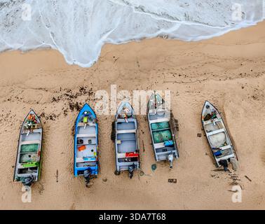 Aus der Vogelperspektive auf die Fischerboote, die am Sandstrand liegen, während türkisfarbene Wellen in der Nähe abstürzen, Facho, Porto, Portugal. Stockfoto