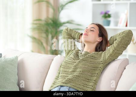 Entspannte Frau in Grün, die zu Hause auf einem Sofa sitzt Stockfoto