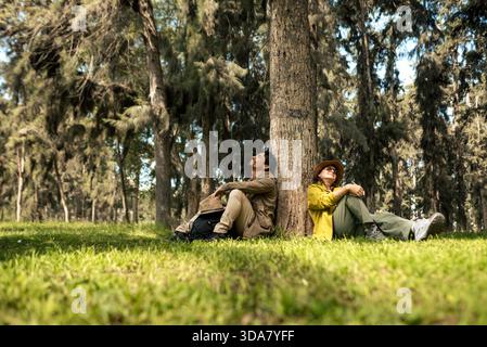 Ein multiethnisches Paar sitzt und ruht an einem Baum im Wald. Stockfoto