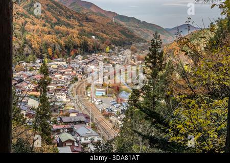 Ein Blick aus der Vogelperspektive auf das Dorf Narai im Kiso-Tal, das die Chuo-Linie entlang des Flusses Narai zeigt, eingerahmt von Bergen mit herbstlichen Farben. Narai ist Teil der Stadt Shiojiri und liegt auf einer Höhe von 900 Metern; die Eisenbahnlinie verbindet Nagoya mit Matsumoto. Shiojiri, Präfektur Nagano, Japan Stockfoto