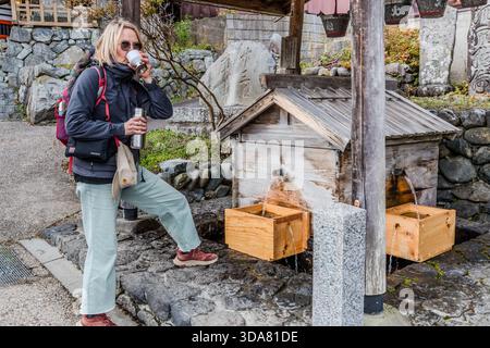 Eine Frau trinkt Wasser aus einem öffentlichen Holzbrunnen (Mizuba) in Narai-juku, Shiojiri, Präfektur Nagano, Japan. Die Brunnen entlang der historischen Nakasendo Post Road lieferten einst Wasser für Wanderer und Reisende auf der Strecke zwischen Edo und Kyoto Stockfoto