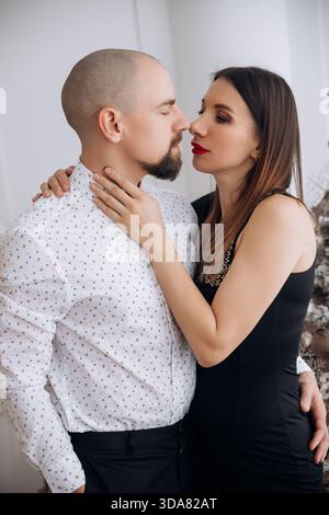 Ein Mann und eine Frau stehen einander nahe und blicken einander in die Augen. Die Frau hat lange dunkle Haare und trägt ein schwarzes Kleid. Der Mann trägt ein li Stockfoto